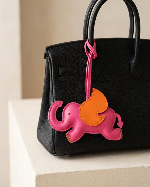 The Elephant Charm in hot pink on a black leather handbag